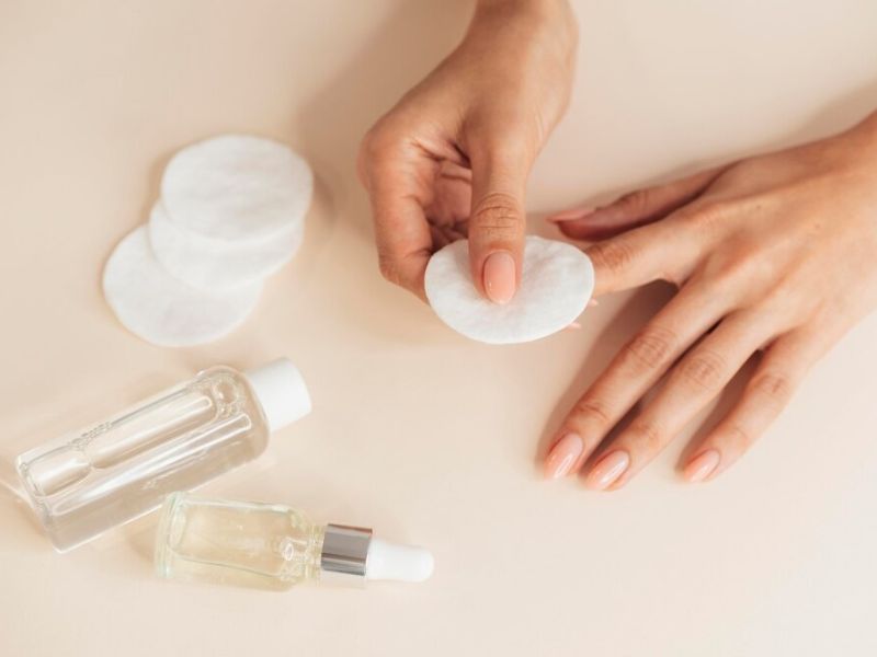 Mulher cuidando da unhas com produtos para remoção de esmalte e hidratação das unhas.